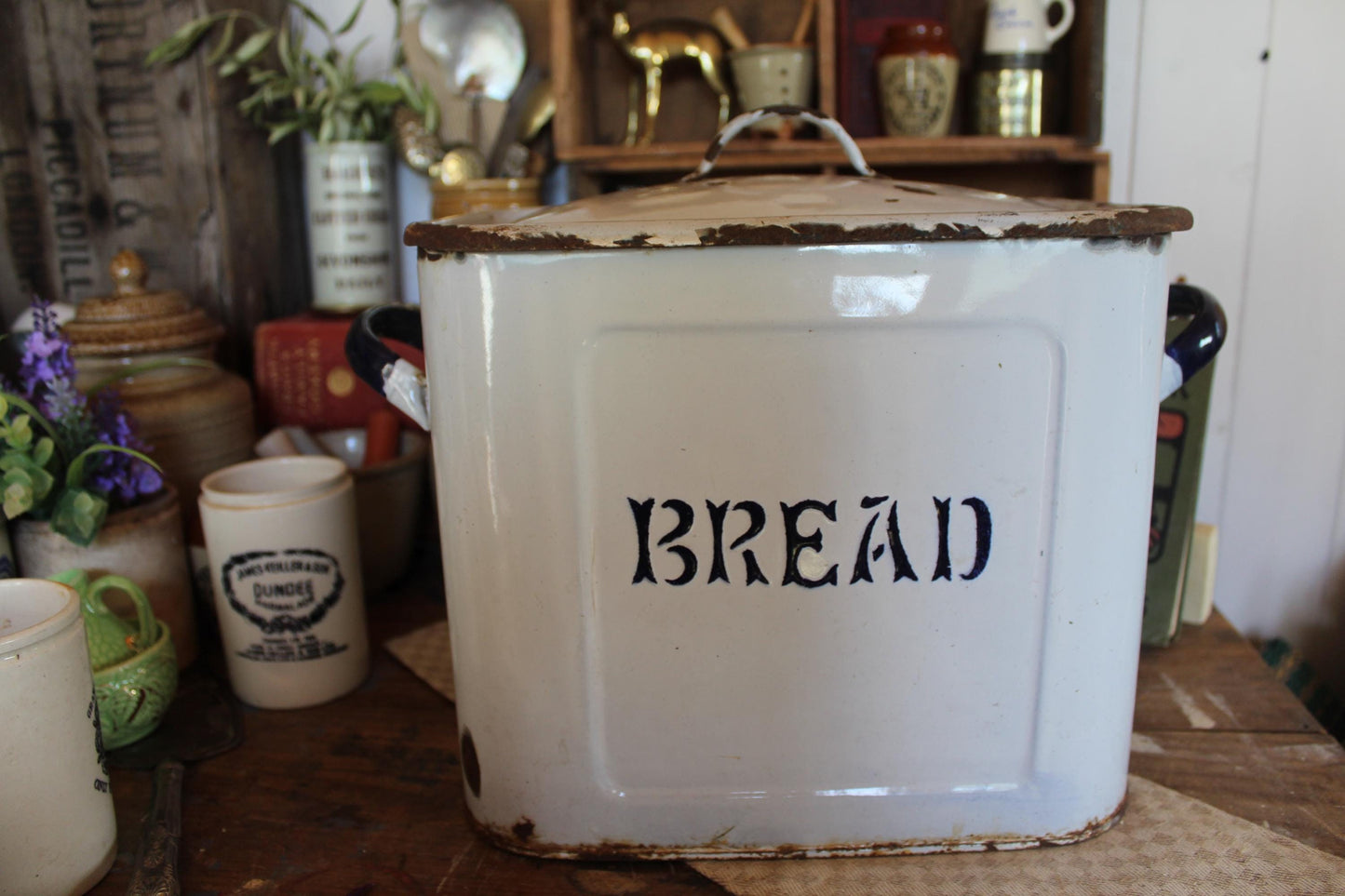 White enamel and blue bread bin with bread written in blue on the front, has handles to the sides and on the lid.