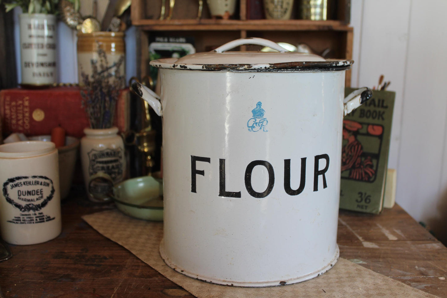 white enamel metal flour bin with handles on the sides and on the lid. Flour stamped in black on the front of the flour bin with the monogram of King George dating to the 1930s